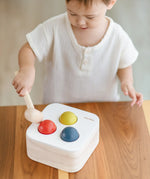 Child playing with the PlanToys punch and drop bin wooden pounding toy. Hammering the red ball into the bin through a slot on the lid.
