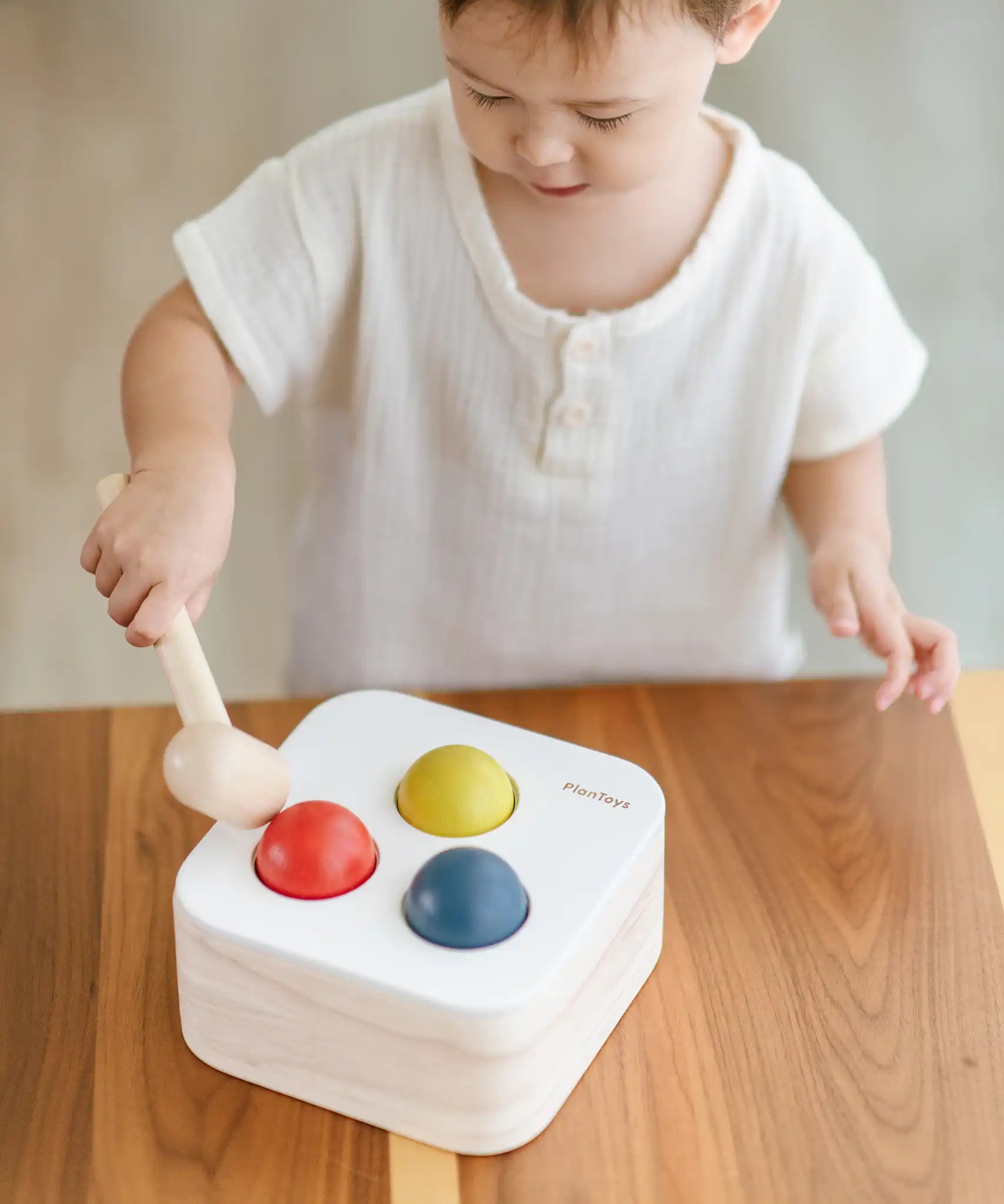 Child playing with the PlanToys punch and drop bin wooden pounding toy. Hammering the red ball into the bin through a slot on the lid.