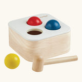 PlanToys punch and drop bin wooden pounding toy. Wooden box with three slots on the top, red, yellow and blue balls with a wooden hammer.
