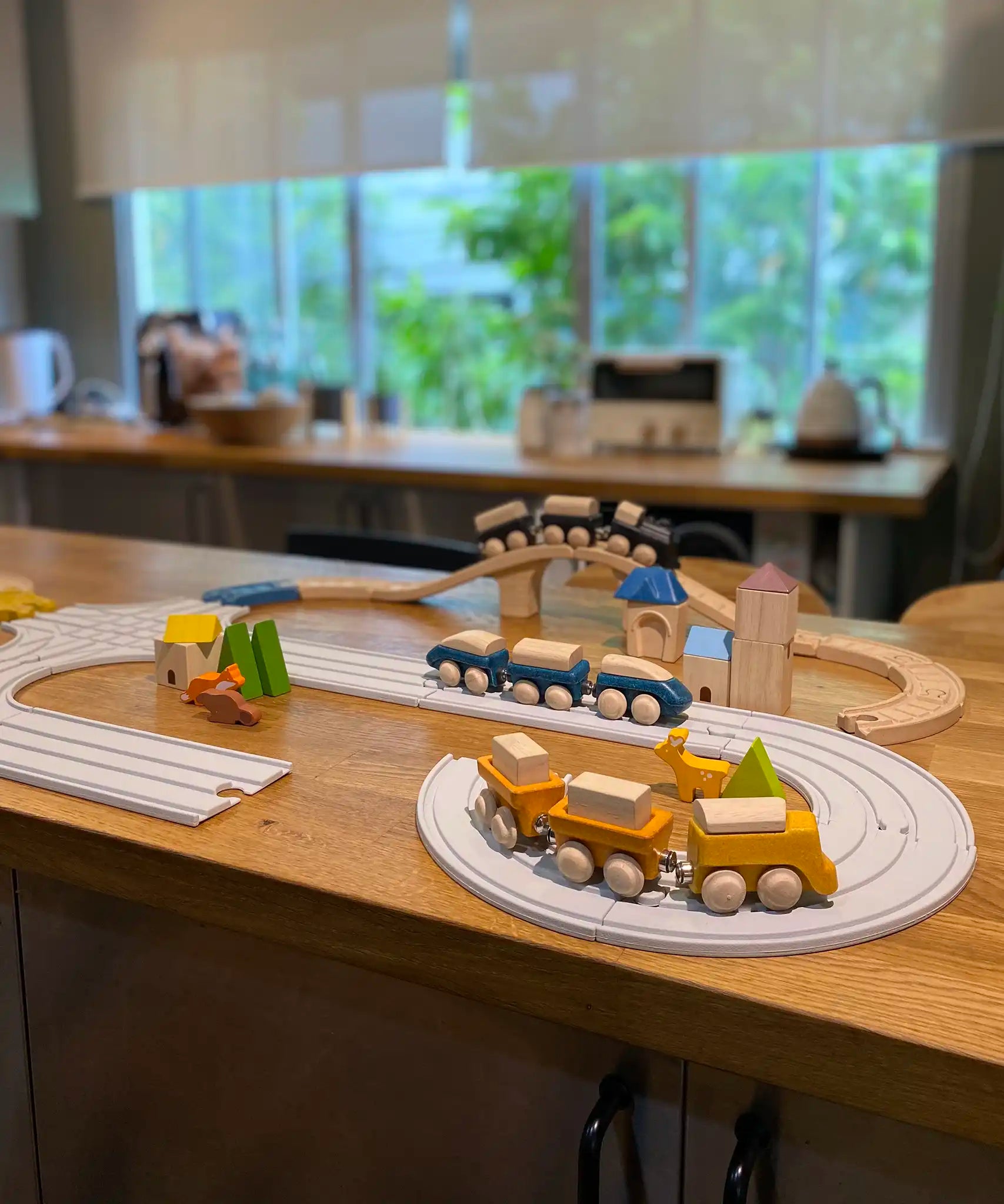 PlanToys wooden trains and blocks placed around the wooden train tracks and rubber railway road sets.