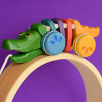 A Plan Toys Rainbow Alligator placed on a natural pieces of a Grimm's rainbow. 