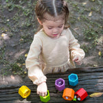 A child playing with the PlanToys Bee Hives Rainbow set outdoors. The bees and hives have been placed on a wooden surface. 