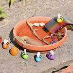 The bees from the PlanToys rainbow bees set being used in a small world play set up outdoors. A terracotta plant stand has been filled with water, some flowers, a stick and a rock. A glass rainbow has been placed on the side with the yellow bee sitting proudly on to.  