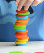 A close up of a child's hand stacking the counters from the Plan Toys Sort & Count Cups set. 