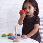 A child playing with the PlanToys Stacking Ring, the child is holding the red ball piece that sits on top of the rod.