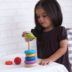 A child playing with the PlanToys Stacking Ring. The child is placing the green piece on the rodded base. 