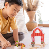 Child playing with the PlanToys barn house small world play set. Red wooden barn, mini veg patch, fences, cow, sheep, hen and farmer figure. 