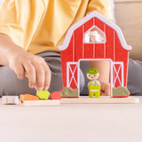 Child playing with the PlanToys barn house small world play set, harvesting a piece of vegetable from the patch. 