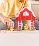 Child playing with the PlanToys barn house small world play set, harvesting a piece of vegetable from the patch. 