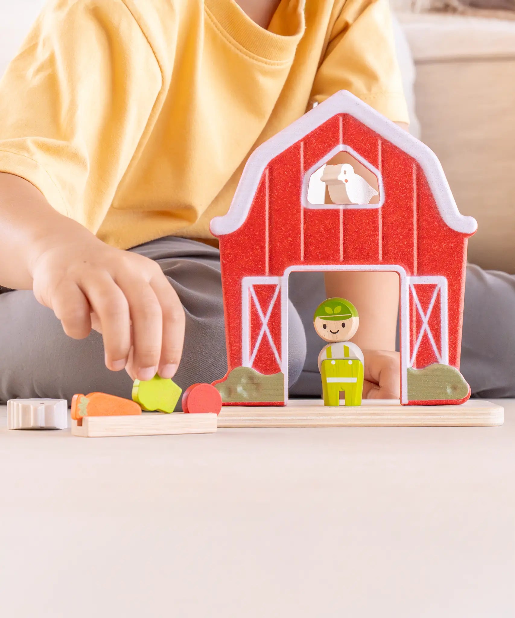 Child playing with the PlanToys barn house small world play set, harvesting a piece of vegetable from the patch. 