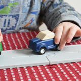 A close up of a blue care on the PlanToys rubber road. A child's hand can be seen pushing the wooden toy car along the road.