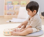 Child playing with the PlanToys wooden sensory drum musical toy, striking the drum with the wood drumstick.