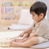 Child playing with the PlanToys wooden sensory drum musical toy, striking the drum with the wood drumstick.