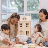 Two toddlers playing with the PlanToys wooden sensory drum musical toy with their parents striking the drums with the wood drumsticks.