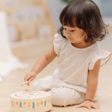 Child playing with the PlanToys wooden sensory drum musical toy, striking the drum with the wood drumstick.