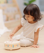 Child playing with the PlanToys wooden sensory drum musical toy, striking the drum with the wood drumstick.