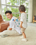 Man sat down on the floor with a child pushing the PlanToys wooden push along sensory massage roller across his back