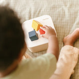 Toddler playing with the PlanToys shape and sort it out bin wooden shape sorter toy placing the shaped blocks into the slots. 