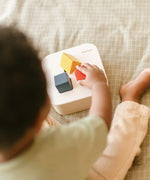 Toddler playing with the PlanToys shape and sort it out bin wooden shape sorter toy placing the shaped blocks into the slots. 