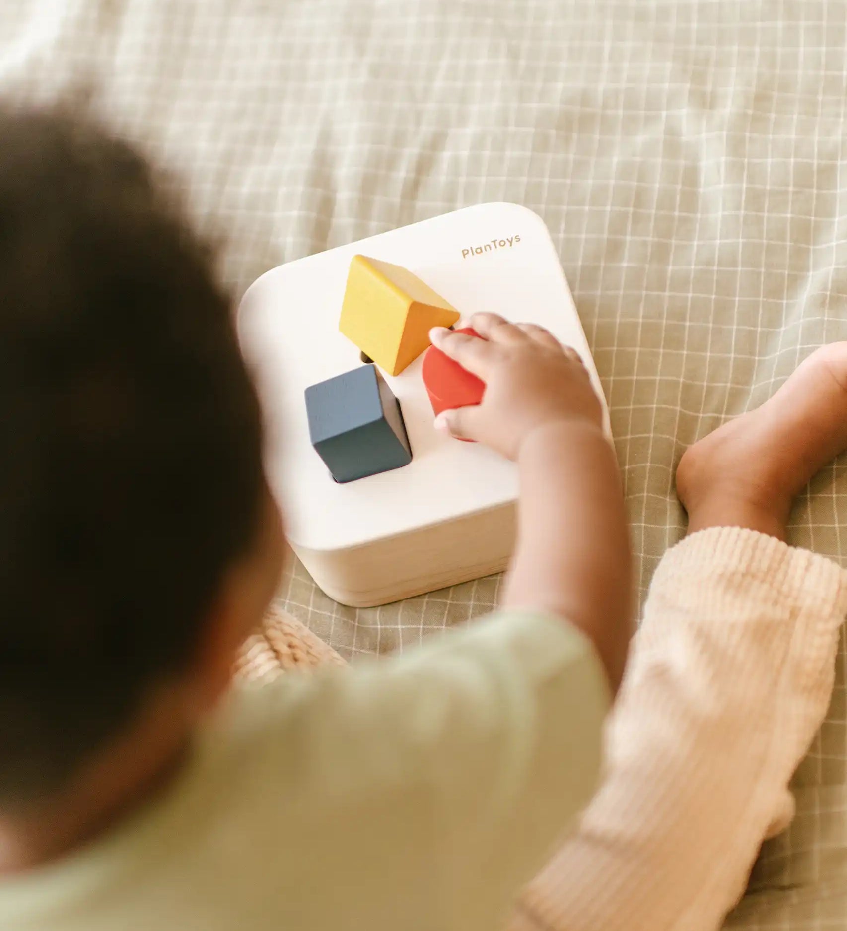Toddler playing with the PlanToys shape and sort it out bin wooden shape sorter toy placing the shaped blocks into the slots. 