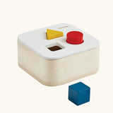 PlanToys shape and sort it out bin wooden shape sorter toy. Square box with lid with three shaped holes in the lid. Yellow triangle, red cylinder and blue cube blocks.