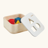 PlanToys shape and sort it out bin wooden shape sorter toy shown with the lid resting on the side. Square box with lid with three shaped holes in the lid. Yellow triangle, red cylinder and blue cube blocks.