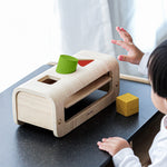 A child playing with the PlanToys Shape and Sort, passing the wooden shape through the peg holes.