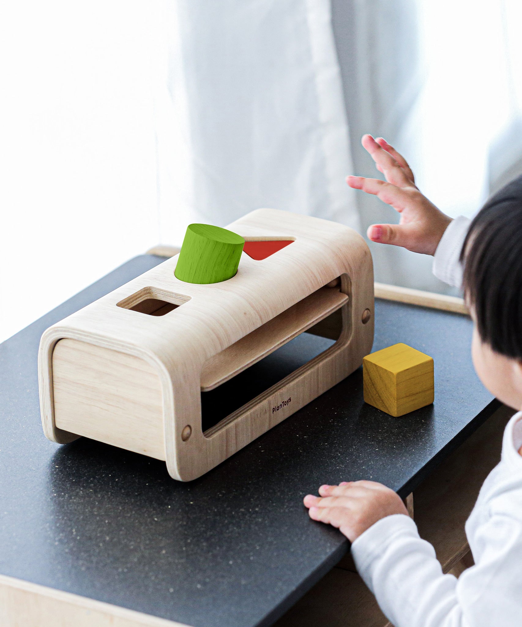 A child playing with the PlanToys Shape and Sort, passing the wooden shape through the peg holes.