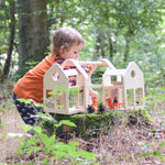 A child playing with the PlanToys Slide N Go Dolls' House placed on a moss covered tree stump in the forest. 
