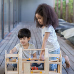 Two children playing with the PlanToys Slide N Go Dolls' House that has been placed on wooden flooring.