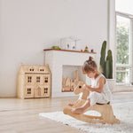 Young girl sat on the PlanToys children's palomino rocking horse on a white fluffy rug in a light playroom