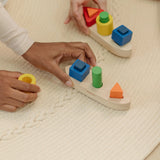 Close up of an adult's hand holding the PlanToys sorting boat wooden shape sorting toy.