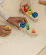 Close up of an adult's hand holding the PlanToys sorting boat wooden shape sorting toy.