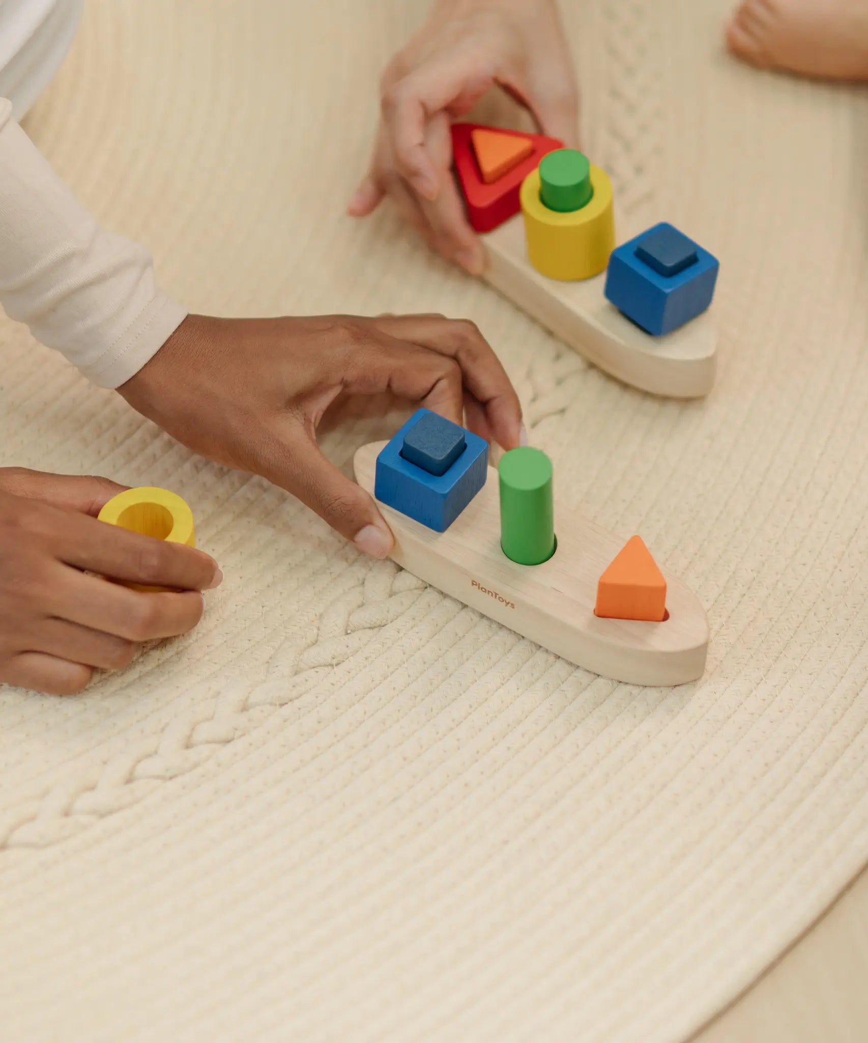 Close up of an adult's hand holding the PlanToys sorting boat wooden shape sorting toy.