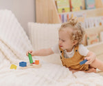 Child playing with the PlanToys sorting boat wooden shape sorting toy, placing the green cylinder onto the base frame.