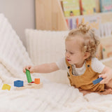 Child playing with the PlanToys sorting boat wooden shape sorting toy, placing the green cylinder onto the base frame.