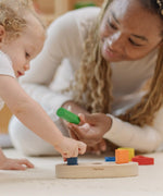 Child playing with the PlanToys sorting boat wooden shape sorting toy with an adult handing them a green cylinder shaped block. 