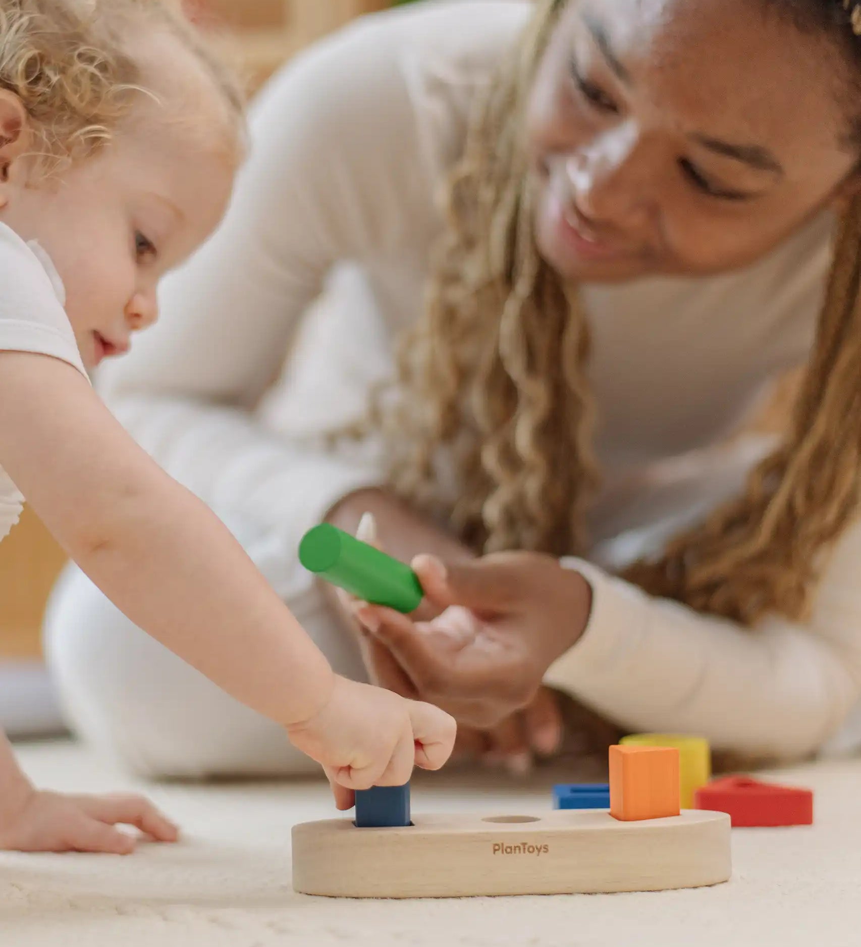 Child playing with the PlanToys sorting boat wooden shape sorting toy with an adult handing them a green cylinder shaped block. 