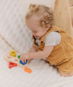 Child playing with the PlanToys sorting boat wooden shape sorting toy placing he blue square piece onto the base.