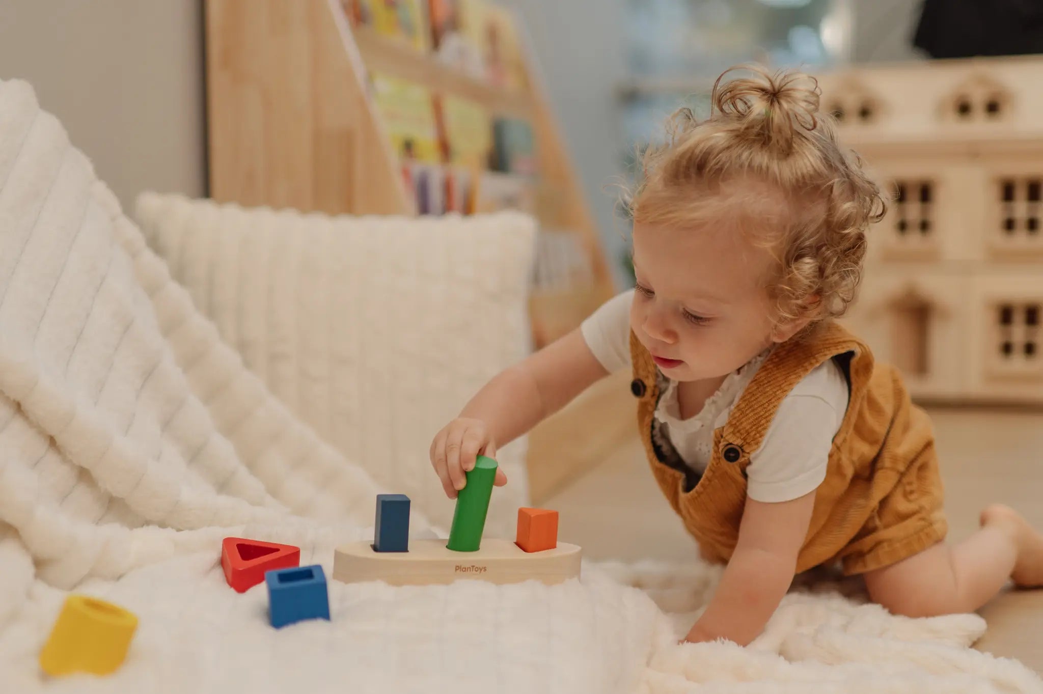 Child playing with the PlanToys sorting boat wooden shape sorting toy, placing the green cylinder pieces onto the base.