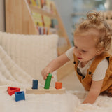 Child playing with the PlanToys sorting boat wooden shape sorting toy, placing the green cylinder pieces onto the base.