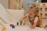 Child playing with the PlanToys sorting boat wooden shape sorting toy, placing the green cylinder pieces onto the base.