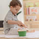 Child lifting up the PlanToys geo sorting bucket wooden shape sorting toy by the rope carry handle.