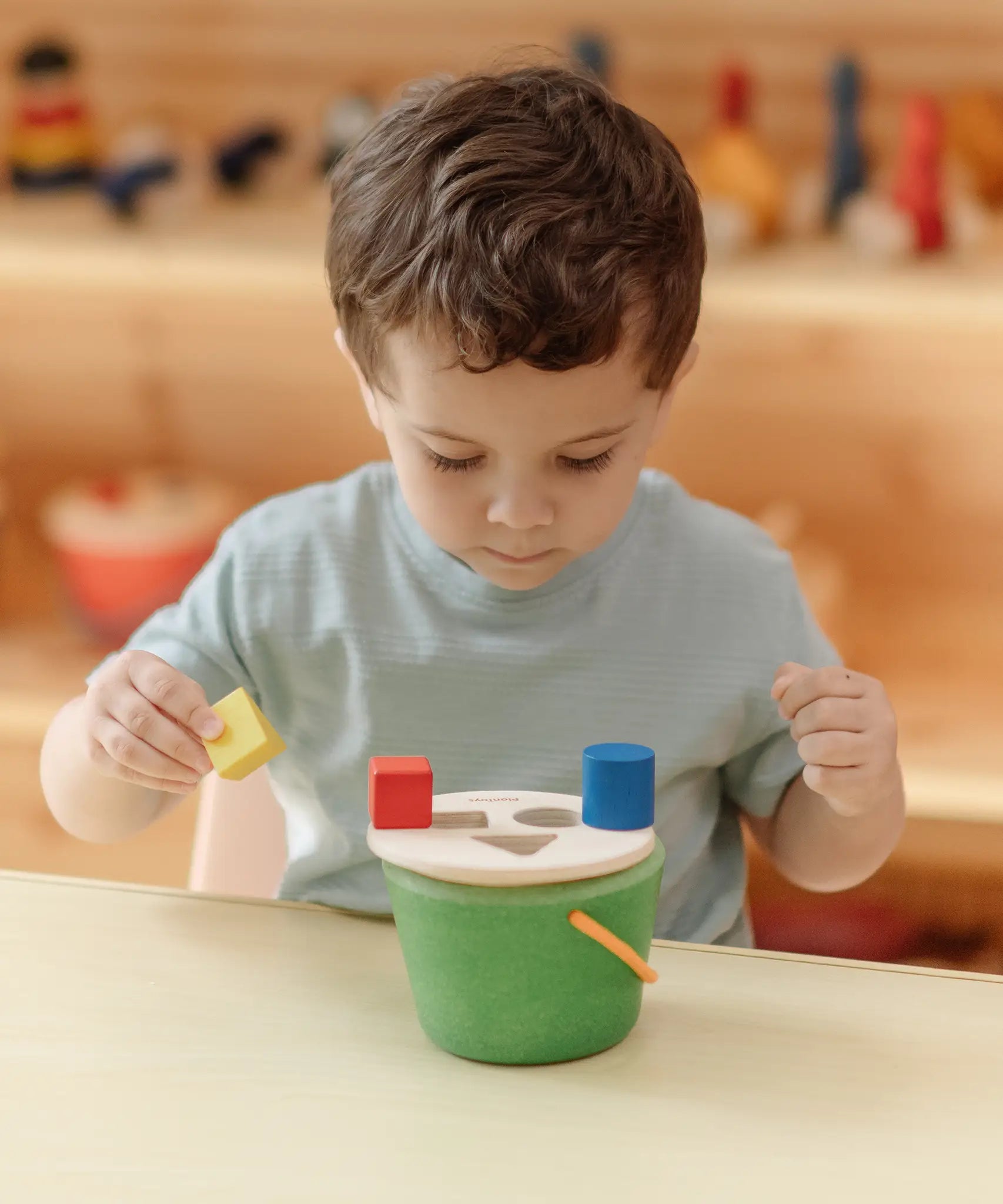 Child placing the coloured wooden blocks on top of the PlanToys geo sorting bucket wooden shape sorting toy. 