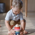 A child crouching down playing with the PlanToys orchard colour way Stacking Rocket Baby Toy.