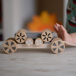 The Plan Toys Stacking Wheels toy, a child's hand can be seen on the side pushing the wheels.