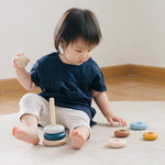 Child sat on a grey carpet playing with the PlanToys plastic-free wooden stacking orchard rings