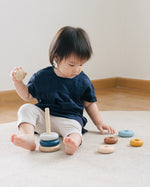 Child sat on a grey carpet playing with the PlanToys plastic-free wooden stacking orchard rings
