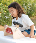 Child playing with the PlanToys Driving Console wooden toy, looking at one of the wing mirrors.