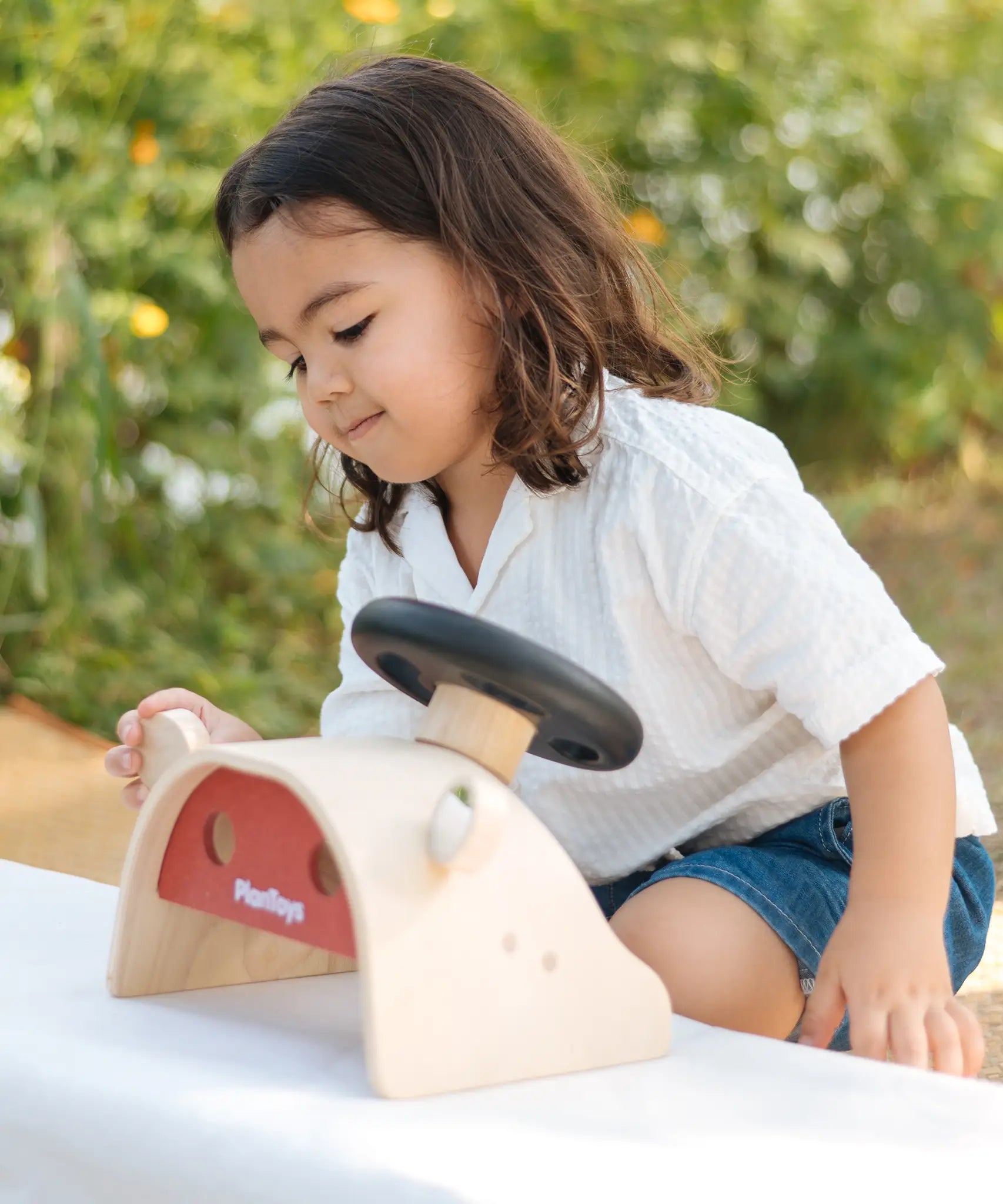 Child playing with the PlanToys Driving Console wooden toy, looking at one of the wing mirrors.